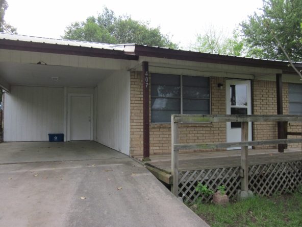 Brick house with carport and wooden deck.