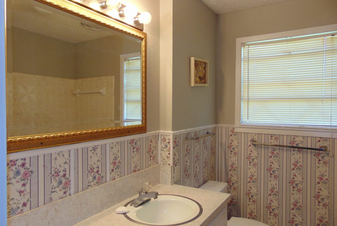 Bathroom sink, mirror, and floral wallpaper.