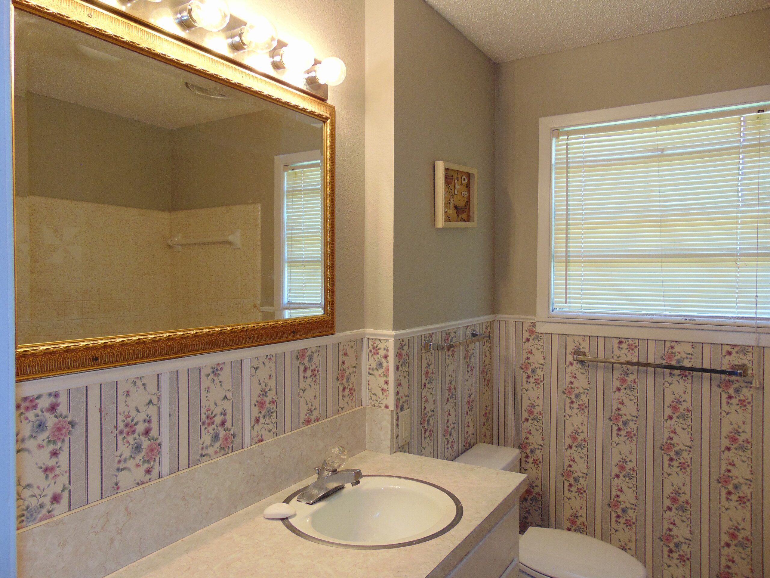 Bathroom sink, mirror, and floral wallpaper.