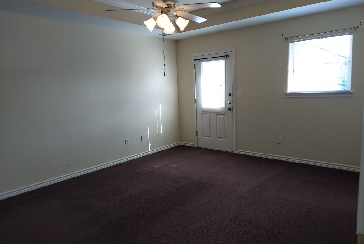 Empty bedroom with dark carpet and ceiling fan.