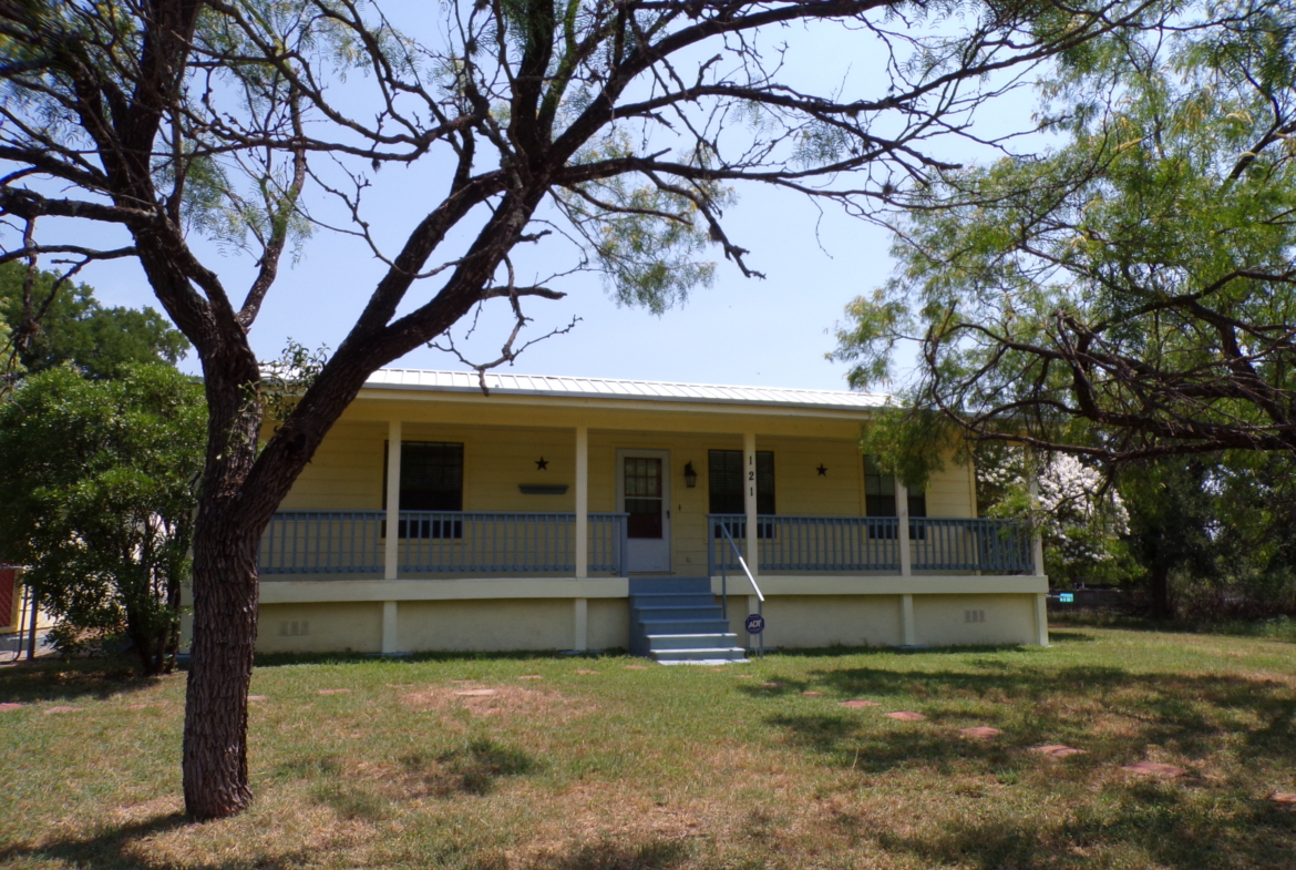 Yellow house with porch and trees.