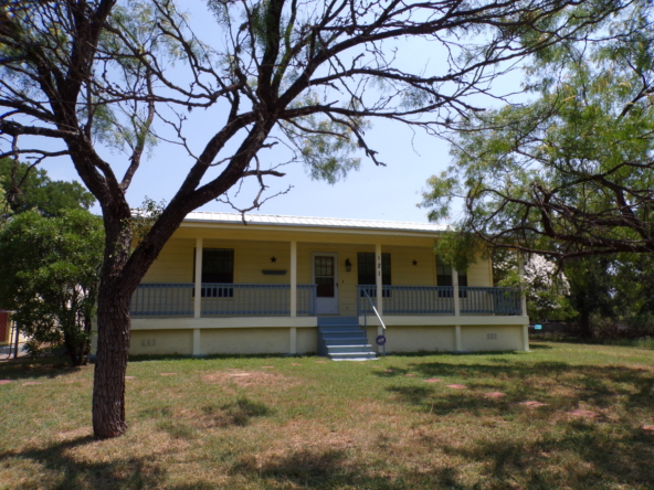 Yellow house with porch and trees.