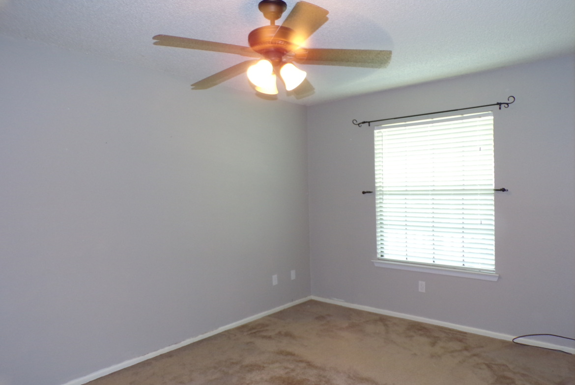 Empty bedroom with ceiling fan and blinds.