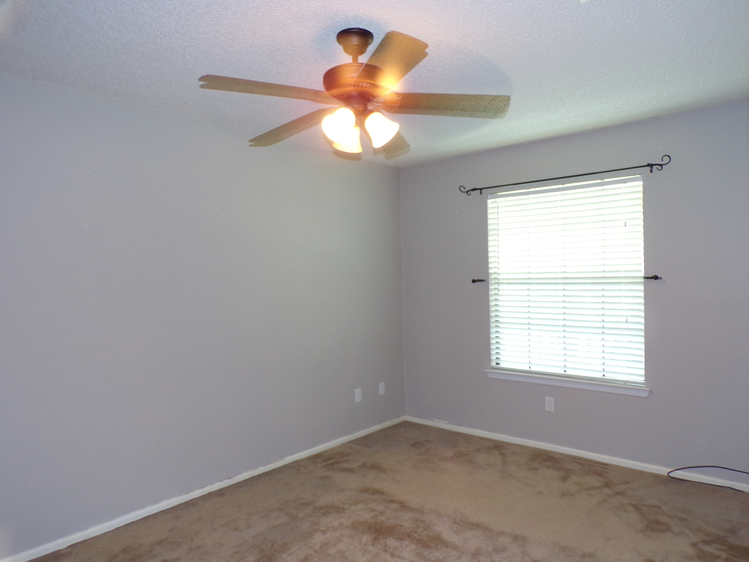 Empty bedroom with ceiling fan and blinds.