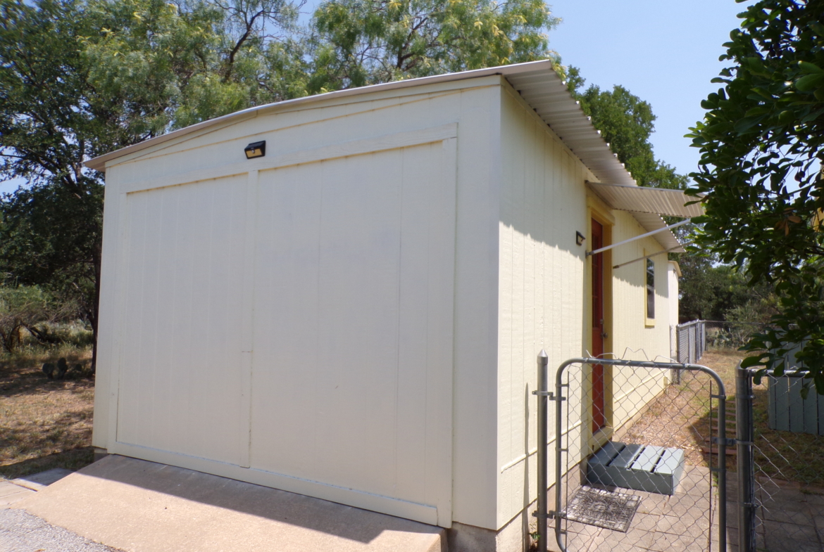 Here's an alt tag for the image: Cream-colored storage shed with gate.