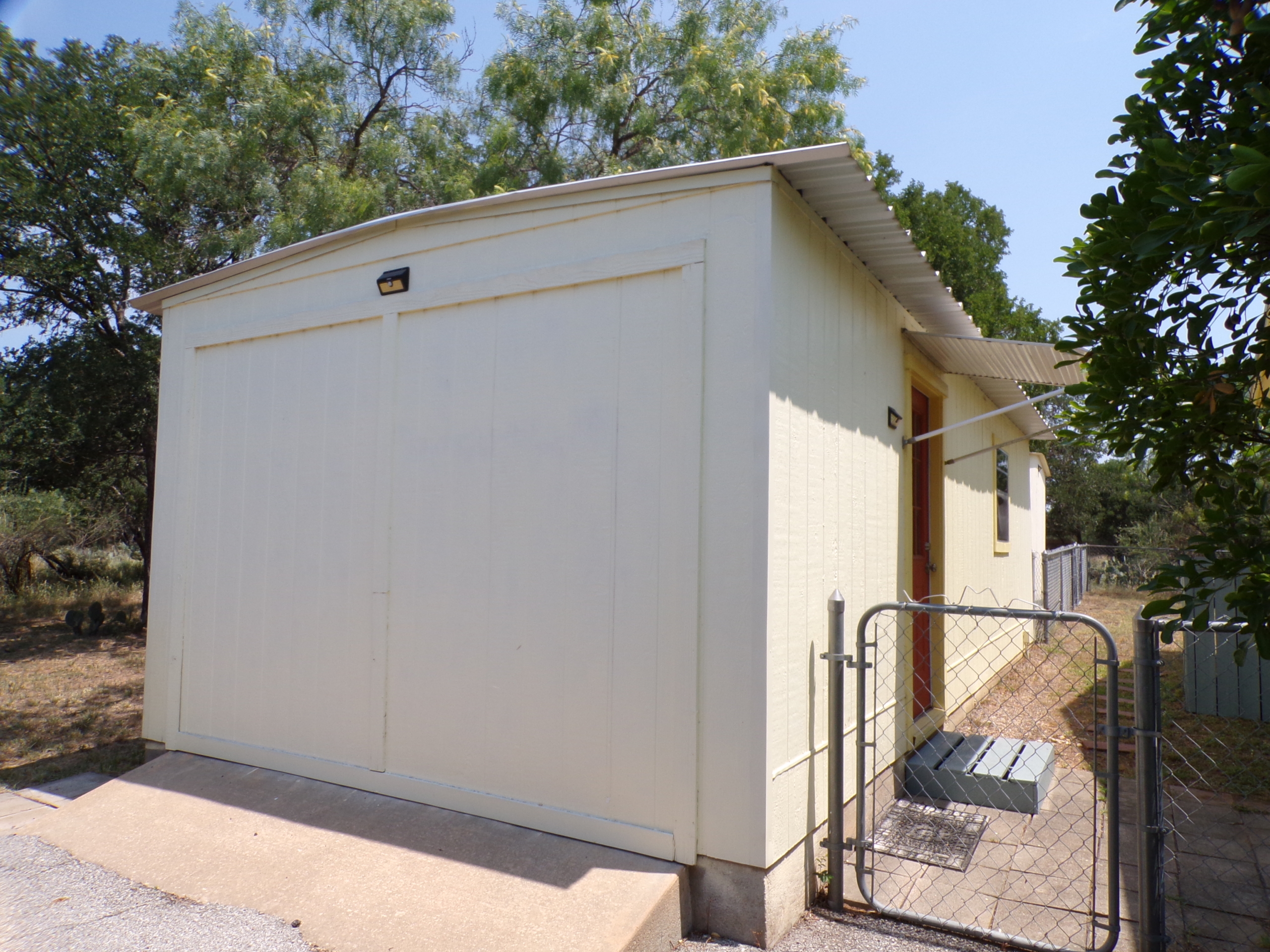 Here's an alt tag for the image: Cream-colored storage shed with gate.