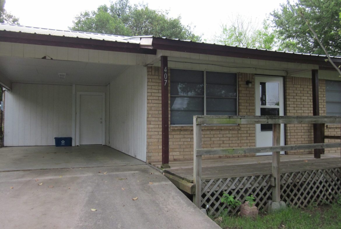 Brick house with carport and wooden deck.