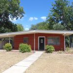 Brick ranch house with carport and lawn.
