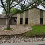 Stone house with green lawn and tree.