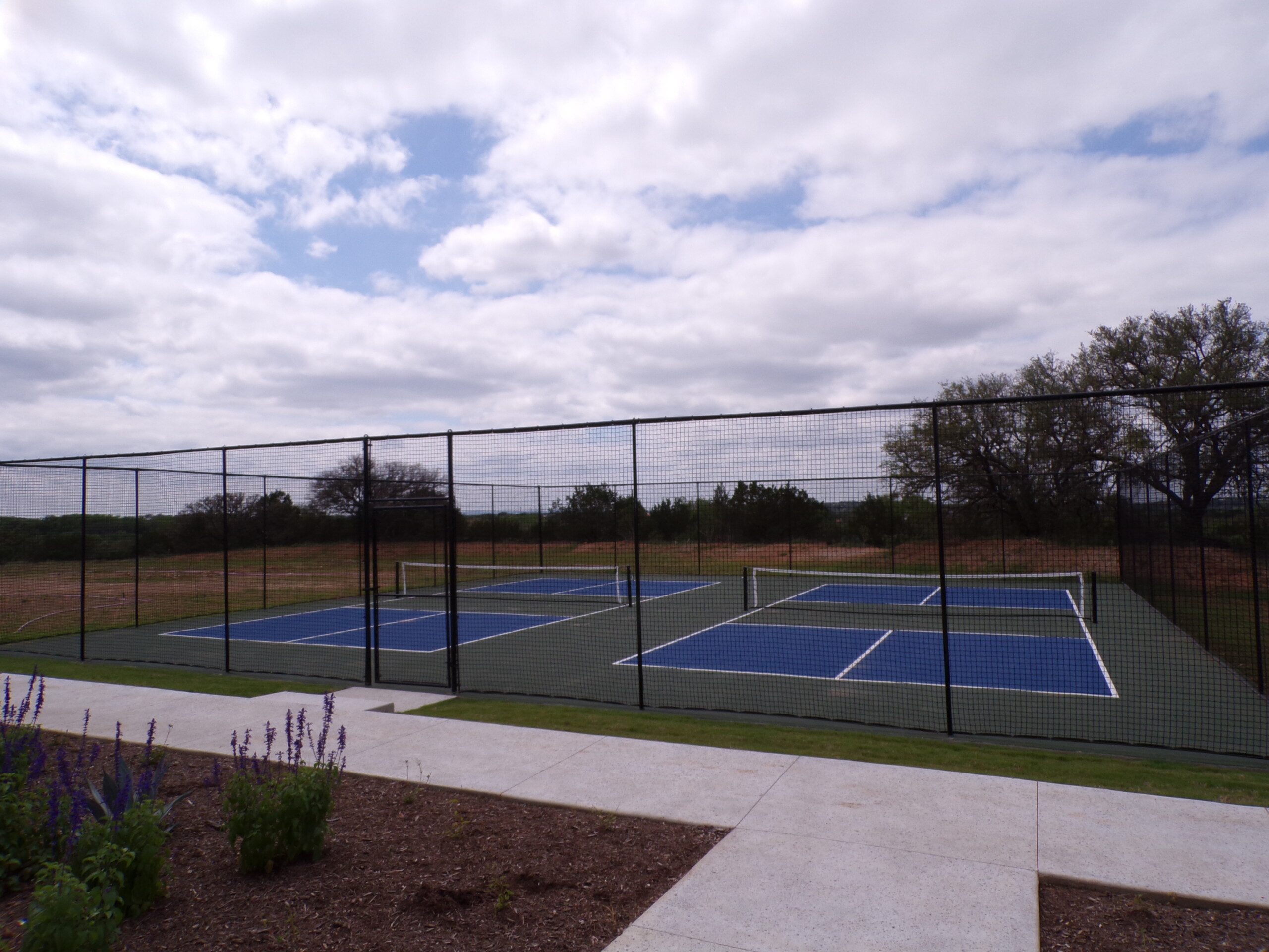 Here's an alt tag for the image: Three pickleball courts outdoors.