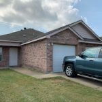 Here's a short alt tag for the image: Brick house with attached garage and truck.