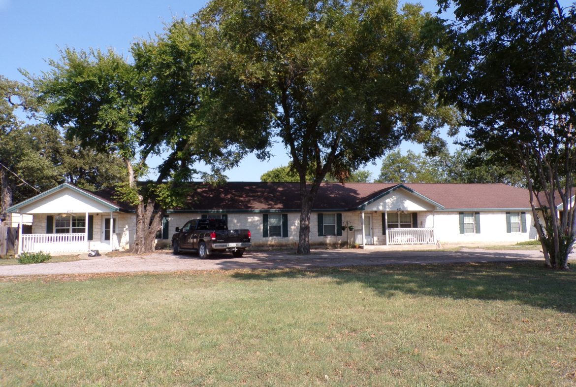 Here's an alt tag for the image: White houses, truck, shady lawn.