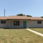 Beige brick ranch house, teal door.