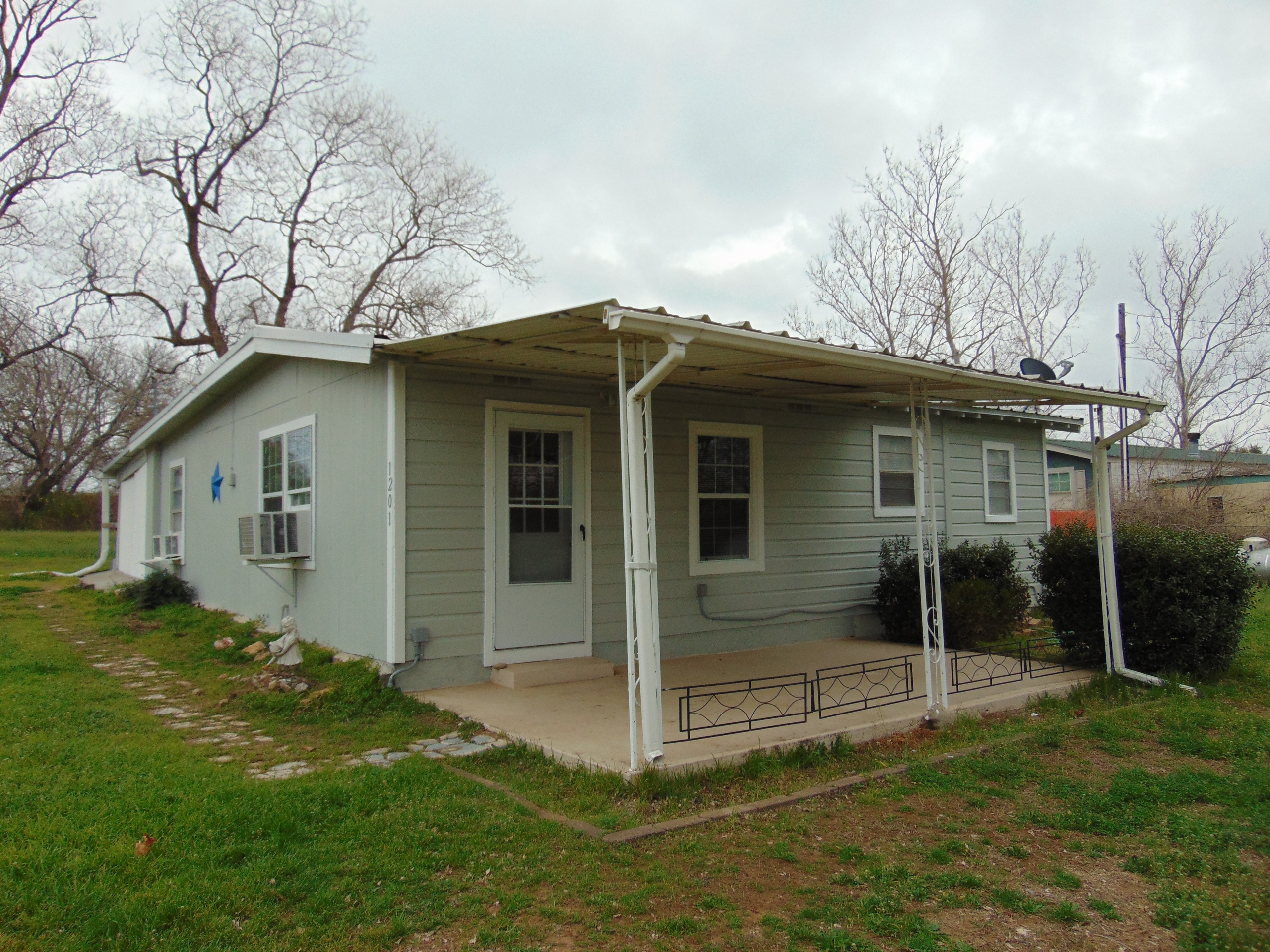 Gray house with covered porch and shrubs.
