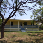 Yellow house with porch and trees.