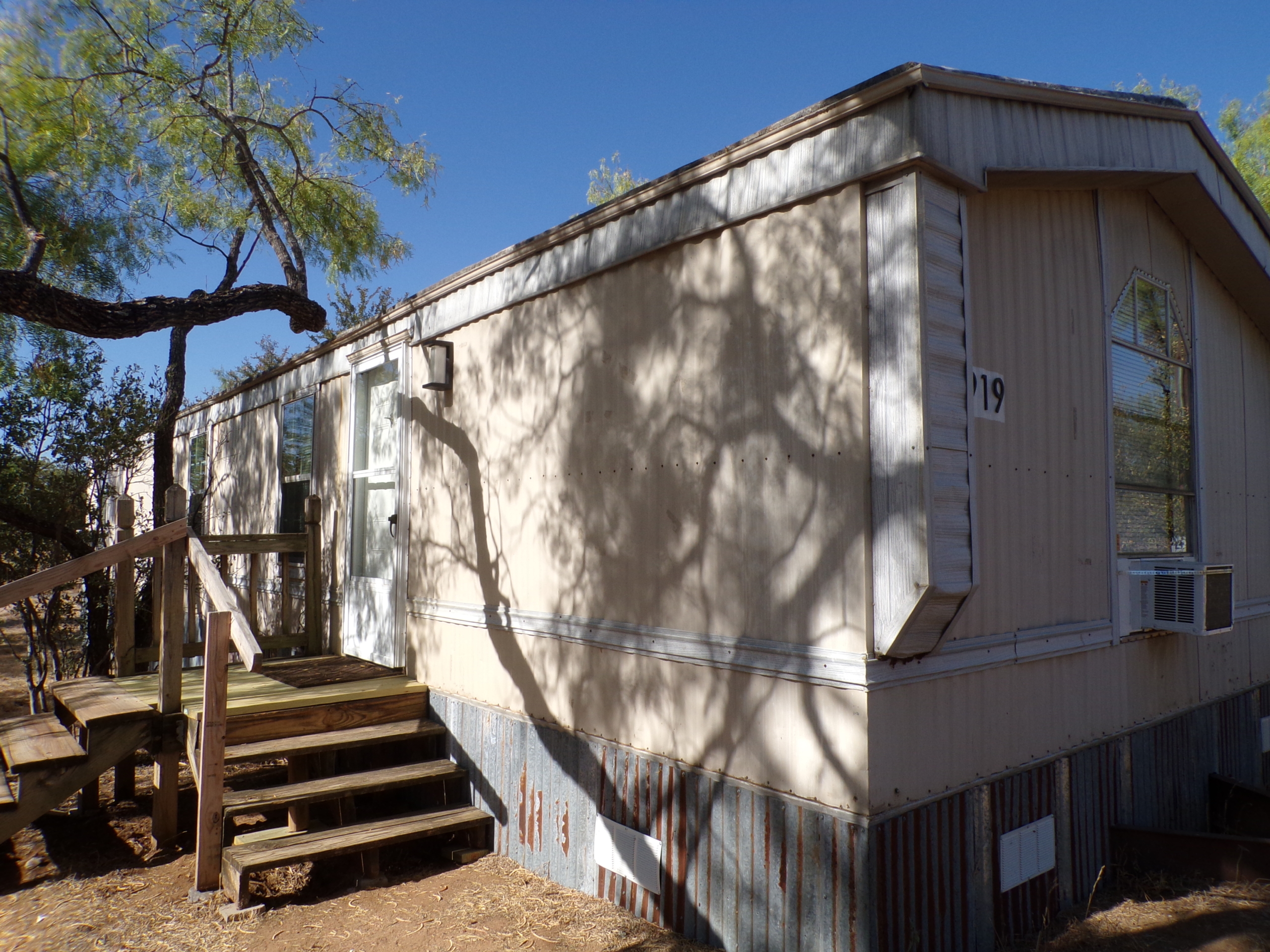 Mobile home number 19, steps, tree shade.