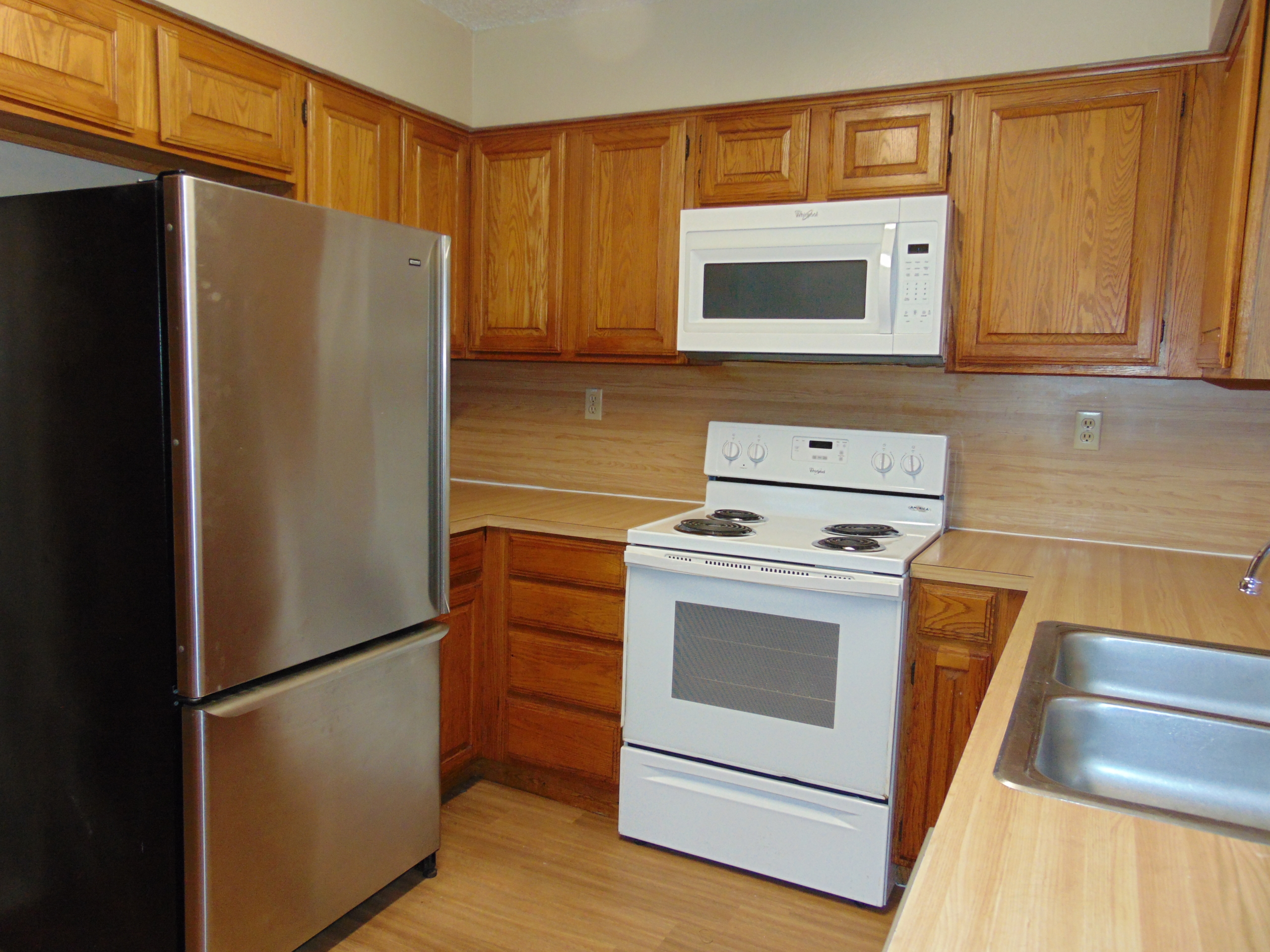 Stainless steel fridge, white stove, wooden cabinets.